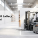 Electric forklift beside a heavy traction battery in a bright warehouse service bay
