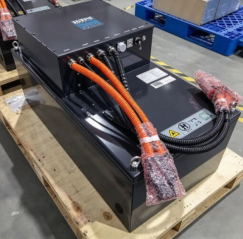 Forklift lithium battery pack with high-voltage orange cables and electrical connectors photographed in a battery manufacturing workshop.